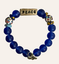 Blue beaded bracelet with 'PEACE' charm on a textured surface